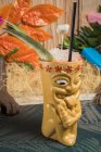 Polynesian tiki cup of cold alcohol beverage decorated with straw and green leaves placed against colorful leaves and dry grass — Stock Photo