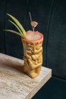 Polynesian tiki cup of cold alcohol beverage decorated with straw and green pineapple leaves placed against on wooden table — Stock Photo