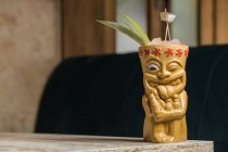 Полинезийская чашка теки холодного алкоголя, украшенная соломой и зелеными листьями ананаса, прижатыми к деревянному столу — стоковое фото