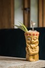Copa tiki polinesia de bebida alcohólica fría decorada con paja y hojas de piña verde colocadas sobre una mesa de madera - foto de stock