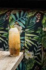 Tiki-Tasse mit kaltem Alkohol-Getränk mit Stroh serviert mit Eis und dekoriert mit frischen Kräutern auf verschwommenem Hintergrund platziert — Stockfoto