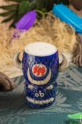 De arriba de la taza tiki en forma de toro de bebida alcohólica con espuma colocada contra hierba seca y plumas sobre fondo borroso - foto de stock