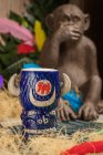 Bull shaped tiki mug of alcohol drink with froth placed against dry grass and feathers on blurred background — Stock Photo