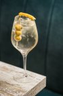 From above of crystal wineglass with Martini cocktail served with lemon zest and olives edge of wooden table — Stock Photo