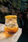 From above of tiki glass mug with booze placed on edge of wooden table in room with colorful curtain on blurred background — Stock Photo