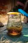 Taza de vidrio Tiki con alcohol colocada en el borde de la mesa de madera en la habitación con hierba seca sobre fondo borroso - foto de stock