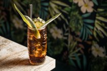 Dall'alto di tazza di tiki di vetro piena di bevanda alcolica con paglia decorata con frutto posto su orlo di divano di tavolo di legno — Foto stock
