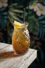 Caneca tiki de vidro preenchida com bebida alcoólica com palha decorada com frutas colocadas na borda do sofá de mesa de madeira — Fotografia de Stock