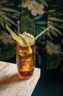 De cima da caneca de vidro tiki preenchida com bebida alcoólica com palha decorada com frutas colocadas na borda do sofá de mesa de madeira — Fotografia de Stock