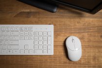 Top view of white modern keyboard and mouse near computer placed on wooden table — Stock Photo