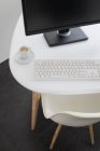 Зверху сучасний комп'ютер з чорним монітором і білою клавіатурою, розміщеною на столі з чашкою кави в офісі — стокове фото