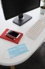 Computer moderno e smartphone con notebook posizionato su tavolo bianco con maschera medica e pianta in vaso in ufficio leggero — Foto stock