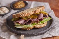 Nahaufnahme eines köstlichen Pastrami, Salat, Schinken und Essiggurken-Sandwich — Stockfoto