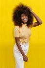 Young cheerful ethnic female with Afro hairstyle touching hair while looking at camera in sunlight — Stock Photo