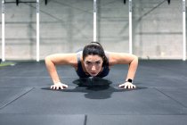 Сильная целеустремленная молодая спортсменка делает отжимания во время интенсивной функциональной тренировки в спортзале — стоковое фото