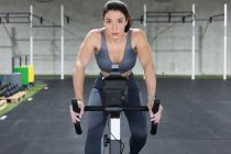Визначений м'язиста жінка-спортсменка в спортивному одязі їзда на стаціонарному велосипеді під час функціональних тренувань у спортивному клубі — стокове фото