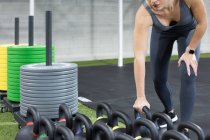 Crop unrecognizable athletic female picking heavy kettlebell while preparing for weight exercise during functional training in gym — Stock Photo