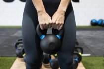 Crop anonymous athletic female in sportswear doing exercises with heavy kettlebell during functional workout in gym — Stock Photo