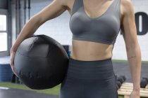 Урожай безликий спортсменка в активному одязі тримає медичний м'яч під час підготовки до вправ під час інтенсивних функціональних тренувань у спортзалі — стокове фото