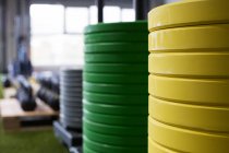Многоцветные тяжелые металлические пластины, сложенные на искусственной траве в современном тренажерном зале с различным спортивным оборудованием — стоковое фото