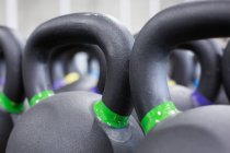 Full frame closeup of heavy black iron kettlebells with colorful weight labels arranged in rows in gym — Stock Photo