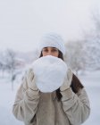 Jeune contenu ethnique femelle en bonnet tricoté montrant boule de neige sous le ciel blanc dans le parc de Madrid — Photo de stock