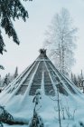 Tenda Sami tradicional colocado na floresta de inverno perto de árvores cobertas com geada e neve contra o céu nublado — Fotografia de Stock