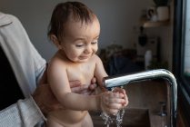 Cultivar pai irreconhecível lavar criança encantada brincando com água da torneira na pia — Fotografia de Stock