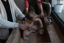 Обрезанная неузнаваемая маленькая девочка, стирающая миленького ребенка на руках отца во время купания в раковине на кухне — стоковое фото