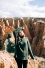 Молодая веселая туристка в теплой одежде и очках стоит напротив ущелья с закрытыми глазами под облачным небом в Испании — стоковое фото