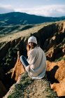 Rückenansicht einer Touristin, die über die Schulter schaut, während sie auf einer Schlucht sitzt und grüne Berge in Spanien betrachtet — Stockfoto