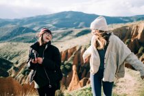 Jóvenes felices viajeros femeninos con cámara de fotos que se divierten contra el monte en el día soleado en la espalda iluminada - foto de stock