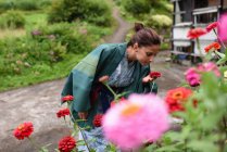 Young attractive caucasian woman in a traditional Japanese kimono smells flowers in garden of small village of Ainokura, Japan — Stock Photo