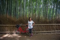 Jolie jeune femme caucasienne avec son vélo regardant les arbres dans la forêt emblématique de Bamboo Grove Arashiyama à Kyoto, Japon — Photo de stock