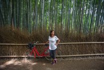 Attraktive junge kaukasische Frau mit ihrem Fahrrad und Blick auf Bäume im Arashiyama Bamboo Grove Wald in Kyoto, Japan — Stockfoto