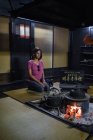 Jeune femme caucasienne agenouillée devant un feu dans une maison traditionnelle japonaise — Photo de stock