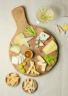Зверху різноманітний нарізаний сир на дерев'яній дошці з грінками, розміщеними на столі — стокове фото
