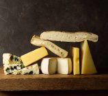 Varios quesos cortados sobre tabla de madera colocados sobre mesa de madera - foto de stock