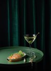 Du dessus de tranches de saumon fumé appétissantes servies dans une assiette avec de la lime et de l'oignon et placées sur une table ronde avec un verre de vermouth avec olive près d'un élégant collier de perles — Photo de stock