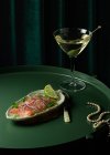 Зверху апетитні шматочки копченого лосося подаються на тарілці з лаймом і цибулею і кладуть на круглий стіл зі склянкою вермута з оливковою олією біля витонченого перлового намиста — стокове фото