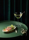Von oben appetitlich geräucherte Lachsscheiben auf Teller mit Limette und Zwiebel serviert und auf runden Tisch mit Glas Wermut mit Oliven in der Nähe elegante Perlenkette gelegt — Stockfoto