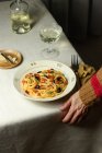 Cortado pessoa irreconhecível comendo Spaghetti alla Puttanesca servidor com vidro oh vinho branco colocado na mesa com guardanapo — Fotografia de Stock