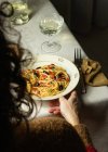 Cortado pessoa irreconhecível comendo Spaghetti alla Puttanesca servidor com vidro oh vinho branco colocado na mesa com guardanapo — Fotografia de Stock