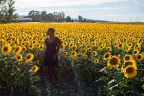 Afroamerikanerin im Kleid steht vor dem Hintergrund blühender Sonnenblumen auf dem Feld und genießt den Sommer in der Natur — Stockfoto