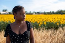 Donna afroamericana in abito in piedi sullo sfondo di girasoli in fiore nel campo e godersi l'estate in campagna — Foto stock