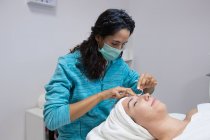 Crop anonymous beautician in mask treating adult woman with closed eyes during facial procedure in beauty center — Stock Photo