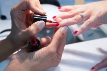 Cultivo irreconocible maestro de belleza femenina aplicando barniz rojo en la uña de la mujer durante el procedimiento de manicura en el centro de spa - foto de stock