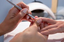 Crop unrecognizable female beauty master applying red varnish on nail of woman during manicure procedure in spa center — Stock Photo