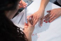 Alto ângulo de corte anônimo beleza mestre arquivamento unha da mulher usando o conselho de esmeril durante o procedimento de manicure na mesa — Fotografia de Stock