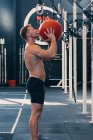 Vista laterale dello sportivo con busto nudo che lancia palla medica durante l'allenamento funzionale in palestra — Foto stock